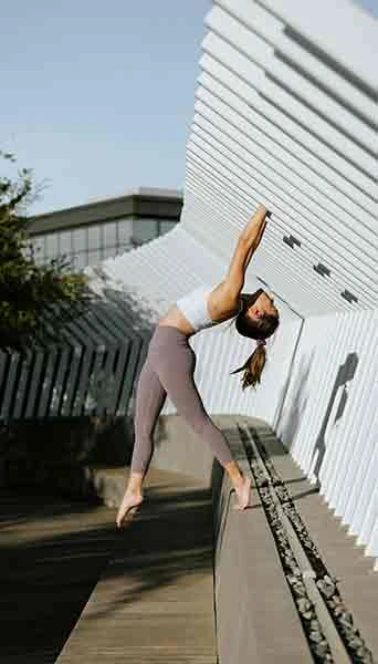 women stretching in a yoga pose against a modern building wall outside