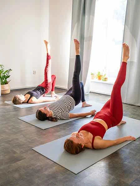 three women doing a pilates exercise on yoga mat demonstrating balance