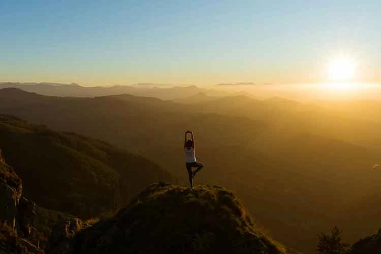 women doing a yoga pose on a mountain sunset landscape